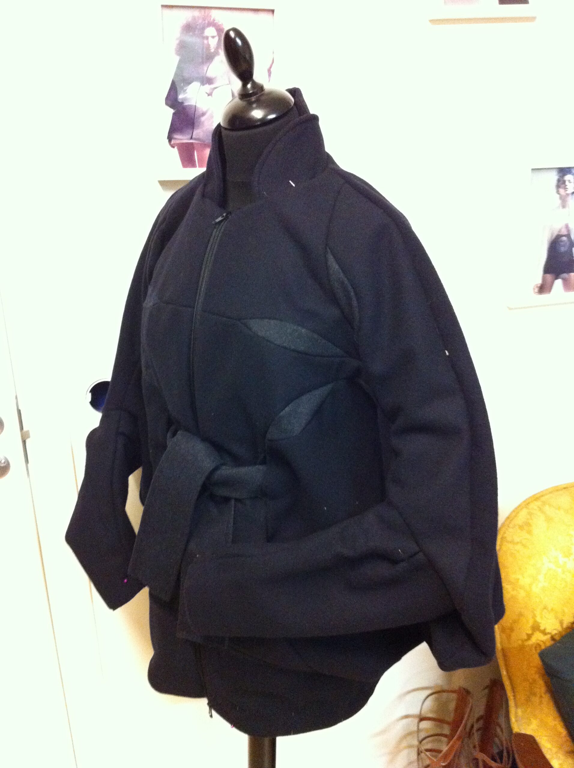Dark belted jacket with an angled front closure on a dress form