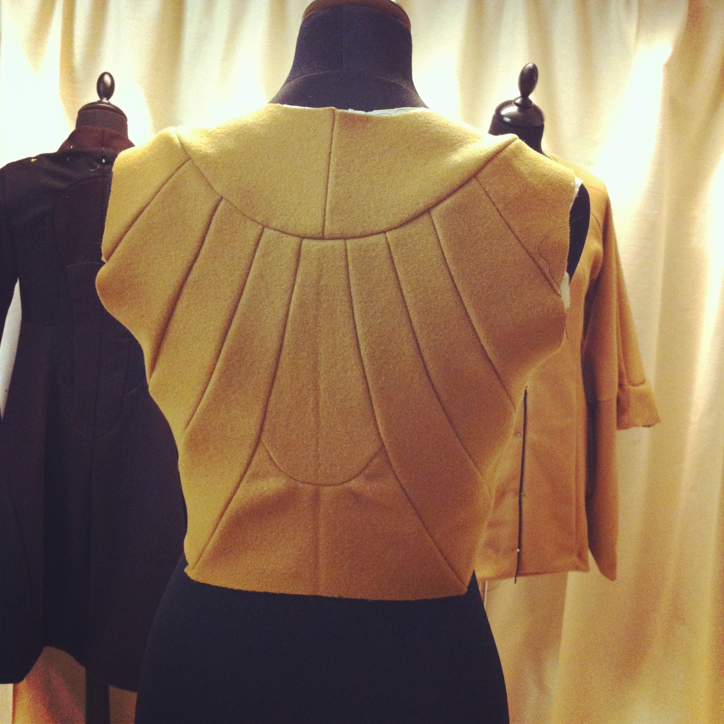 Rear view of a gold-toned sleeveless garment with radiating panels on a dress form