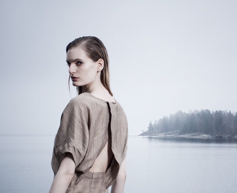 Model wearing an open-backed neutral dress beside water