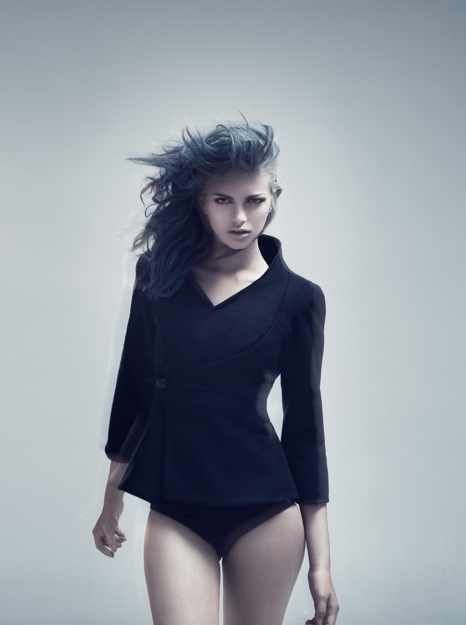 Model wearing a fitted black jacket with an asymmetric front against a pale background