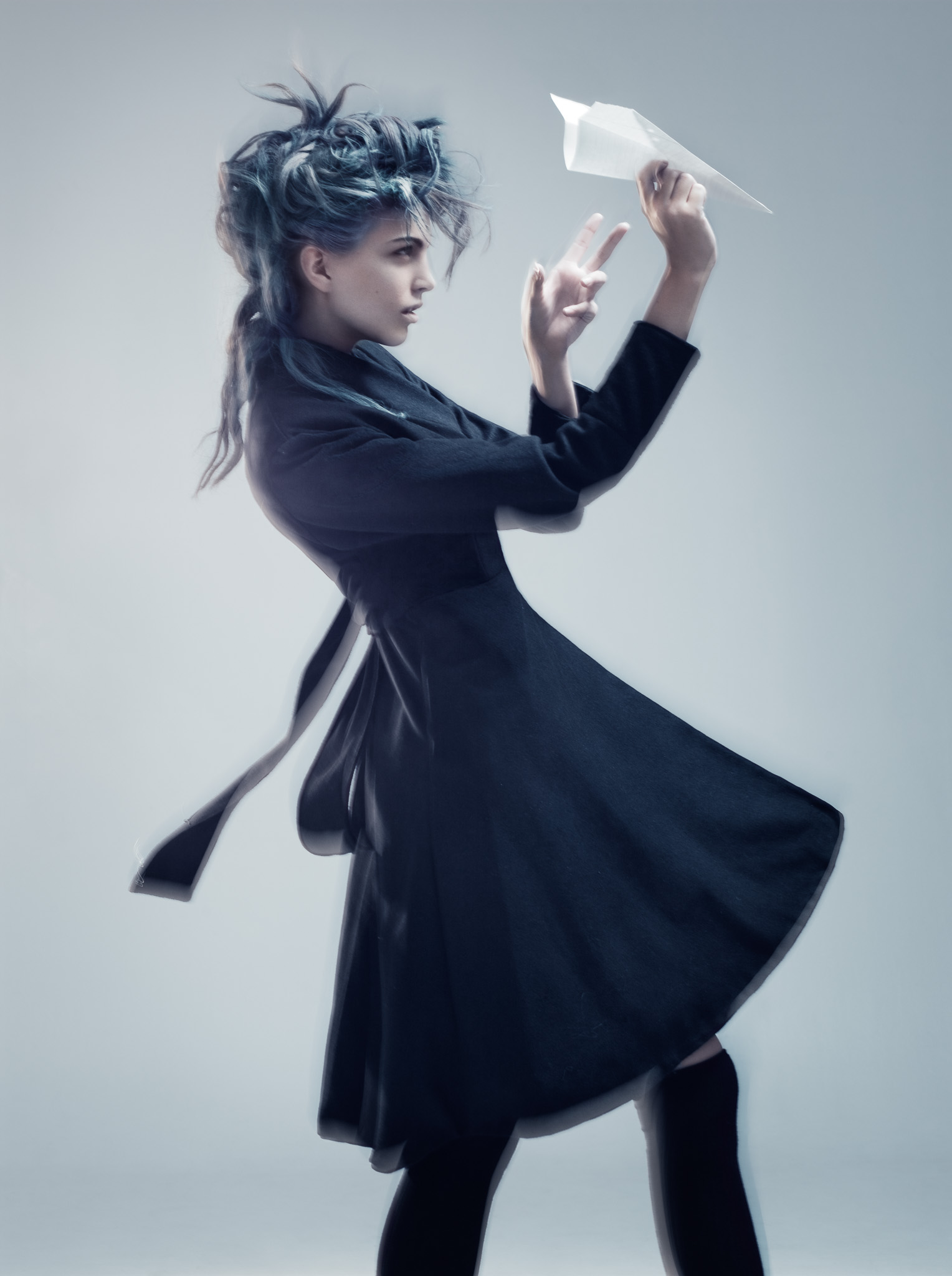 Model in a dark flared coat, photographed in motion against a pale background