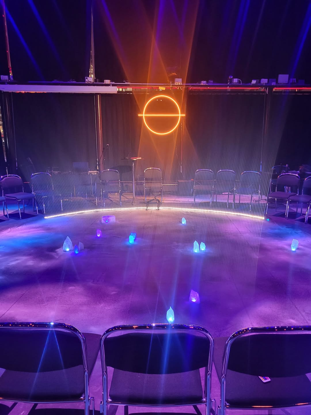 The empty AfroStar Galactica performance space has a circle of chairs, blue floor lights and an orange circular sign.